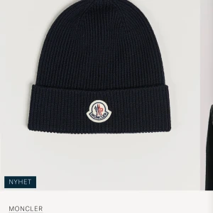 Marinblå ribbad mössa från Moncler - Snygg marinblå mössa från Moncler med ribbad struktur och uppvikt kant. Framtill sitter Monclers klassiska logotyp i vitt, rött och blått. Perfekt för dig som vill ha en stilren och varm accessoar till vintern. Knappt använd, finns inget kvitto då jag fått i present men den är äkta. 