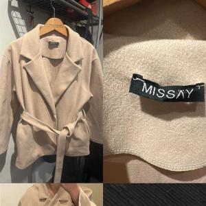 Beige kappa med bälte från Missay - Snygg beige kappa från Missay i mjuk polyester. Jackan har klassisk krage, knytskärp i midjan och en rak, lite loose passform. Perfekt för dig som gillar stilrena och enkla plagg med en modern touch.