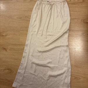 Satinkjol - Snygg beige långkjol från Nelly i mjukt satinmaterial. Kjolen har elastisk midja med snörning!💛 Aldrig använd 