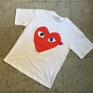 Vit Cdg Play t-shirt - Säljer en vit t-shirt från Cdg Play med stort tryck och logga framtill i storlek S, oanvänt skick och fraktas inom 24h✅