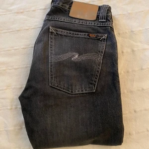 Mörkgråa jeans från Nudie - Snygga mörkgråa jeans från Nudie med klassisk femficksdesign och kontrastsömmar på bakfickan. Jeansen har slim fit passform och är tillverkade i mjukt bomullsmaterial. Perfekt för dig som gillar stilrena och tidlösa jeans med coola detaljer. Hör av dig vid intresse eller frågor! Modellen är Grim Tim😍