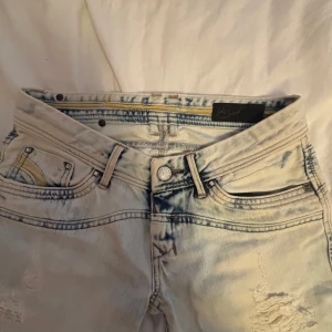 Ljusblå slitna jeans från Salsa - Säljer ett par ljusblå jeans från Salsa med slitna detaljer framtill och bakfickor med gul dekor. Jeansen har låg midja och raka ben. Perfekta för en avslappnad och trendig look. Straight men bootcut up till person till person 