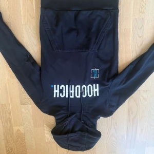 Svart set från Hoodrich med tryck - Svart set från Hoodrich med stor vit logga och blå detalj på bröstet. Texten 'PRODUCT OF THE STREETS' på ena ärmen och känguruficka framtill. Huva med snörning och mjukt bomullsmaterial. Perfekt streetwear-vibe.