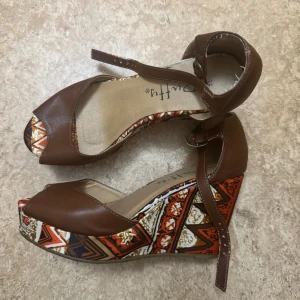 Bruna kilklackade sandaler med mönster - Snygga bruna sandaler med kilklack och öppen tå, storlek 36, använd ett fåtal gånger men finns lite slit däremot inget som syns på utsidan. 