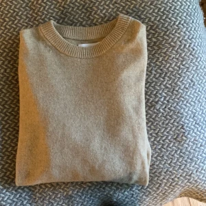 Beige stickad tröja från Samsøe Samsøe - Snygg beige stickad tröja från Samsøe Samsøe med rund hals och ribbade muddar vid ärmslut och nederkant. Perfekt för dig som gillar stilrena och enkla plagg. Långärmad och i mjukt material som känns skönt mot huden.