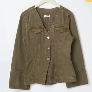 Olivgrön jeansjacka med knappar - Snygg olivgrön jeansjacka med markerad midja och v-ringad hals. Jackan har långa ärmar, två bröstfickor med lock och silverfärgade knappar framtill. Perfekt för dig som gillar en stilren och avslappnad look.