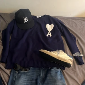 Marinblå stickad tröja från Ami - Snygg marinblå stickad tröja från Ami med stort vitt hjärta och bokstaven A på bröstet. Rund hals och ribbade muddar vid ärmslut och nederkant. Perfekt för dig som gillar stilrena detaljer och vill ha något som sticker ut. Scick 9/10 säljer då den va för stor. priset är ej hugget sten och hör av er vid funderingar