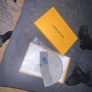 Grå mössa i ull - Snygg grå mössa med klassiskt rutigt mönster. Tillverkad i mjuk ull och levereras med originalförpackning. Perfekt accessoar för att lyfta din vinterstil.