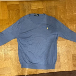 Blå v-ringad tröja från Polo Ralph Lauren - Mycket snygg blå v-ringad tröja från Polo Ralph Lauren med klassisk gul broderad logga på bröstet!🙌