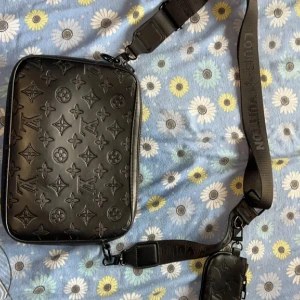 Svart L7 axelväska - Snygg svart axelväska i skinn med klassiskt monogrammönster. Väskan har justerbar axelrem med logga och en mindre avtagbar ficka. Säljs pågrund av ingen använde