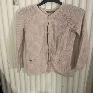 Ljusrosa kofta med fickor - Säljer en söt ljusrosa stickad kofta från Lindex med v-ringning, knappar framtill och två små fickor. Perfekt för lager på lager och passar till många outfits. Långärmad och mjuk i materialet.