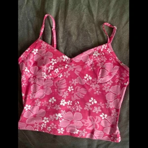 Rosa blommig linnetopp  - Säljer en rosa linnetopp med blommönster i vitt och ljusrosa. Toppen har smala axelband som går att justera, lätt croppad passform och markerade kupor. Den är stretch i så den är S men passar M oxå. Den är lite som baddräkt-material så skönt på sommaren