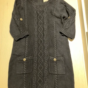 Mörkblå stickad klänning Mayoral Jeans - Mysig mörkblå stickad klänning från Mayoral Jeans med flätstickat mönster, två fickor framtill med knappar och en snygg dragkedja i ryggen. 