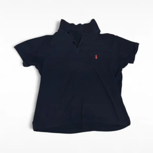 Marinblå pikétröja från Ralph Lauren - Klassisk marinblå pikétröja från Ralph Lauren med korta ärmar och röd broderad logga på bröstet. Tröjan har krage och knäppning framtill. Perfekt för en stilren och sportig look.