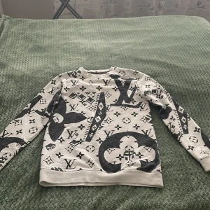 Vit Louis Vuitton sweatshirt S - Säljer en vit sweatshirt från Louis Vuitton i storlek S med ikoniskt svart LV-mönster över hela tröjan. Tröjan har rund hals, långa ärmar och en loose passform. Perfekt för dig som vill sticka ut med en lyxig och trendig look.