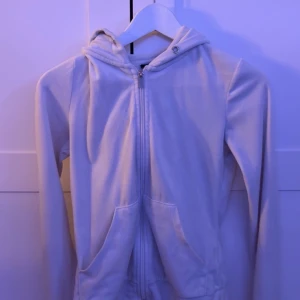 Vit hoodie med dragkedja och huva - Säljer en vit hoodie med dragkedja framtill och praktisk huva. Tröjan har långa ärmar och två fickor på framsidan. 