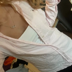 Ljusrosa randig skjorta från GANT - Säljer en ljusrosa skjorta från GANT i storlek 38 men är i storlek S eller Xs i min åsikt. Skjortan har tunna vita ränder, klassisk krage och knäppning framtill. Långärmad och i mjuk bomull, perfekt till jeans eller kjol. Superfräsch och stilren vibe! Skjortan passar lika bra på mig som på en kille då jag sett min kille i den. Passade otroligt bra!