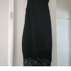 Svart klänning med spetsdetalj - Snygg svart klänning med asymmetrisk nederkant och bred spetskant längst ner.