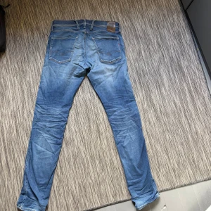 Blå Replay Anbass jeans, stl 31 - Säljer ett par blå Replay Anbass jeans i klassisk tvätt. Jeansen har fem fickor, snygga slitningar och detaljer med kontrastsömmar. Märkespatch i läder baktill och diskret Replay-brodyr vid fickan. Perfekt passform och stilren look. 3 effekter som syns på bilden. Syns men inte tydligt i användning. Jeansen behöver kärlek! Kan diskutera pris. 