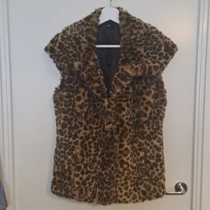 Leopardmönstrad pälsväst  - Fluffig pälsväst från äldre H&M i leopardmönster. Västen har bred krage. Materialet är syntetpäls med mjukt foder. "Snoddar" i sidorna för att kunna ha ett skärp runt midjan. Har en hake som fram för stängning. Har även två små fickor fram 🩷