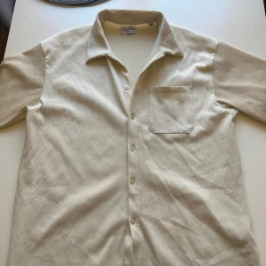 Beige ribbad skjorta Jack & Jones - Snygg beige skjorta från Jack & Jones Originals med ribbad struktur och korta ärmar. Skjortan har klassisk krage, knappstängning framtill och en bröstficka. Perfekt för dig som gillar stilrena och enkla plagg med lite extra känsla.