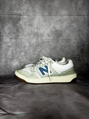 New Balance 480 - Säljer ett par fräscha New Balance sneakers i vitt med blå detaljer och logga. Skorna har snörning, platt sula och rund tå. Ovandelen är i mesh och mocka, med inslag av skinn. Perfekt för dig som gillar klassisk stil med sportig vibe.