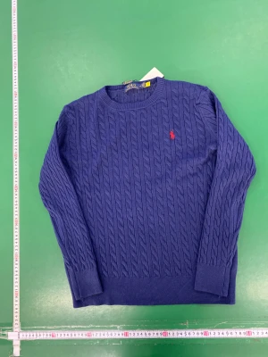 Blå kabelstickad tröja Polo Ralph Lauren - Snygg blå kabelstickad tröja från Polo Ralph Lauren i storlek XL. Tröjan har rund hals, lång ärm och klassisk röd Polo-logga broderad på bröstet. Mjuk och skön känsla, perfekt för dig som gillar stilren design med lite preppy vibe.