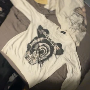 Vit sweatshirt från Dsquared2 med tryck - Säljer en vit långärmad sweatshirt från Dsquared2 med ett stort svart tryck av en döskalle och logga på framsidan. Tröjan har klassisk passform och ribbade muddar vid ärmslut och hals. Perfekt statement piece för dig som gillar streetstyle.skriv om du vill ha bättre bilder!!!