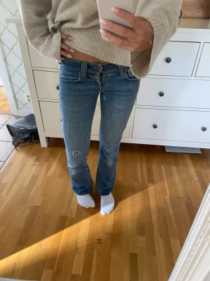 Blå bootcut jeans med slitningar - Snygga blå vintage jeans från fornarina  med bootcut-modell och låg midja. Jeansen har slitningar på ena knät, fransiga benslut för fick sy upp de först för att de var för långa men sen blev de för korta så fick sprätta upp det. Fina Detaljerade bakfickor. Perfekta för dig som gillar avslappnad stil. Älskade de när de inte blev för korta för mig!
