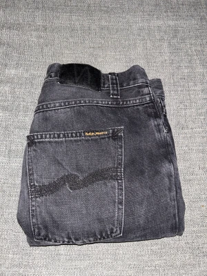 Svarta Nudie Jeans - Snygga svarta jeans från Nudie Jeans med klassisk femficksdesign och raka ben. Jeansen har knappgylf och bälteshällor, tillverkade i slitstarkt denim. Perfekta för dig som gillar en elegant stil. Hör av er vid intresse/ frågor!