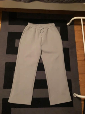Grå mjukisbyxor Saint Alexander S - Grå mjukisbyxor från Saint Alexander i storlek S. Byxorna har elastisk midja med snörning, raka ben och en bakficka med broderad logga. Mjukt material som är skönt att ha på sig, perfekt för chill dagar. Snygg och enkel design. Byxorna är helt nya, säljer de pga att de inte passade. Storlek S men är lite stora i storleken. Flera bilder kan lösas bara att höra av sig och pris kan diskuteras vid snabb affär.