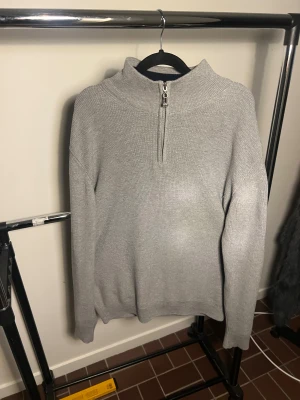 Grå half zip stickad tröja Stone Island - Snygg grå stickad tröja från Stone Island med half zip och hög krage. Tröjan har lång ärm och klassisk Stone Island patch på vänster ärm. Insidan av kragen är marinblå för en schysst kontrast. Perfekt för dig som gillar streetwear och vill ha något stilrent. Storlek XXL men skulle säga XL då den passar perfekt på brorsan