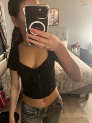 Svart croppad topp med knyt  - Supersnygg svart croppad topp med korta ärmar och knyt framtill. Toppen har en ribbad, och en söt v-ringning som ger en feminin vibe. Perfekt att styla med jeans eller kjol för en trendig look. Köpt utomlands på en marknad. Har aldrig använt förutom på bilden 