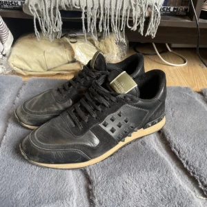 Svarta Valentino Rockrunner sneakers - Svarta Valentino Rockrunner sneakers med coola nitar på sidorna och svart snörning. Ovandel i skinn och mocka, beige sula och diskret logga på plösen. Perfekta för dig som vill ha en edgy och lyxig look. Några av nitarna saknas och syns inte på bild så skicka ett meddelande om bilder innan du köper 
