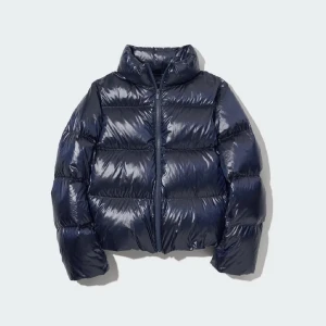 Mörkblå pufferjacka från Uniqlo - Säljer en mörkblå pufferjacka från Uniqlo med glansig finish och hög krage. Jackan har en oversize passform, dragkedja framtill och är riktigt lätt men ändå varm. Fickorna har dragkedjor, men det finns ett litet hål på insidan av höger ficka, det är dock så litet att ingenting kan ramla igenom. 