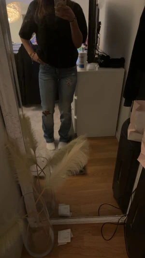 Blå bootcut jeans med slitningar - Säljer ett par blå bootcut jeans med slitningar på knät och lätt tvättade detaljer. Jeansen har klassisk femficksdesign och broderade bakfickor. Snygg passform som sitter tajt upptill och släpper vid benslutet. Perfekta för en avslappnad och trendig look.