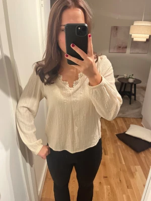 Krämvit blus med spetsdetalj från Vila. - Superfin krämvit blus från H&M med v-ringning och spetskant vid halsen. Långärmad modell i lätt, strukturerat tyg som ger en luftig känsla. Perfekt att styla med jeans eller kjol för en chic look.