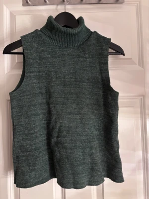 Grön stickad polotopp från Zara - Säljer en mörkgrön stickad polotopp från Zara i storlek S. Toppen är ärmlös med en hög, ribbad polokrage och har en loose passform. Perfekt för lager-på-lager och snygg att styla med jeans eller kjol. Materialet är mjukt och ger en chill vibe.