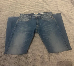 Replay jeans - Snygga blå jeans från Replay med klassisk femficksdesign och raka ben. Jeansen har ljusare tvättade partier framtill och bak, samt Replay-logga på bakfickan och läderpatch i midjan. Perfekt för dig som gillar stilrena och tidlösa jeans.