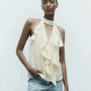 Slutsåld Zara blus med volang - Tja, säljer en krämvit blus med snygg omlott-design och volangdetaljer framtill. Blusen är ärmlös och har en hög halsringning. Toppen har utgått från Zara och säljs inte längre men säljs nu pågrund av att den inte är min stil längre och har aldrig kommit till användning vilket gör den oanvänd. Toppen är perfekt för en kväll ute eller fest. 