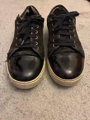 Lanvin skor - Lanvin sneakers i svart mocka med snygg lackad tå och vita gummisulor. Klassisk rund tå, snörning med svarta skosnören och metallöglor. Snygg kontrast mellan mocka och blankt lack framtill. Perfekt för dig som gillar stilrena och lyxiga detaljer. Nya skosnören på. Pris kan diskuteras vid snabbaffär, samt öppen för byten. Tveka inte på att höra av er vid frågor eller funderingar!
