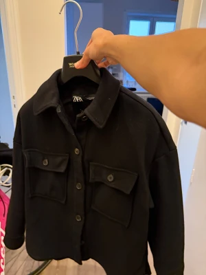 Svart overshirt från Zara - Svart overshirt från Zara med klassisk krage, stora bröstfickor med knappar och knappstängning framtill. Jackan har en loose passform och är långärmad, perfekt för lager på lager. Materialet är mjukt och känns som ullblandning. Xs men känns som small (oversize) 
