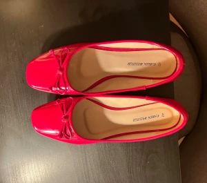 Röda ballerinaskor med rosett - Snygga röda ballerinaskor från Carin Wester med glansig finish och fyrkantig tå. Skorna har en söt rosettdetalj framtill och platt sula🍒🍒