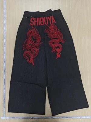 Extrem baggy Wide jeans SHIBUYA med drakbrodyr - Unika svarta jeans med breda ben och hög midja från RVE CHAIN. På baksidan finns röd broderad SHIBUYA-text och två detaljerade drakar. Materialet är robust denim och byxorna har klassisk femficksdesign. Perfekt för dig som vill sticka ut med cool streetstyle.