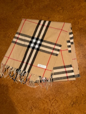 Burberry halsduk  - Säljer denna snygga och nichiga Burberry halsduk som är väldigt lång och stor. Både varm och skön!