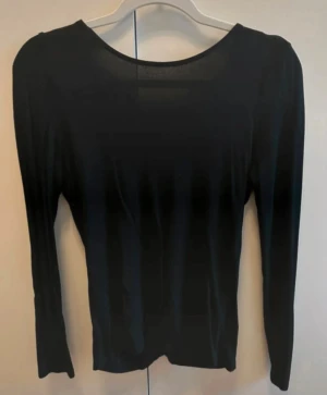 Svart omlottopp med v-ringning - Säljer en snygg svart omlottopp med lång ärm och snygg v-ringning baktill. Materialet är mjukt och stretchigt, perfekt för dig som gillar stilrena och trendiga plagg