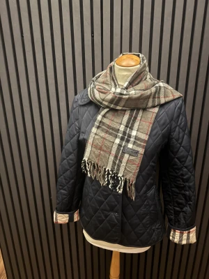  quiltad Berrbery Scarf med rutig detalj - Snygg mörkblå quiltad Scarf med rutiga detaljer. Scarfen har ett klassiskt snitt och är perfekt för dig som gillar stilrena och tidlösa plagg. Quiltad design ger extra värme och en cool look. Passar dig som vill ha något både praktiskt och trendigt.