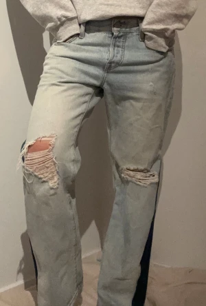 Ljusblå jeans med mörkblå patch - Säljer ett par ljusblå Levi's jeans med slitna hål på båda knäna och en mörkblå patch längs utsidan av benen. Midjemått rakt över: 41 cm Innerbenslängd: 70 cm