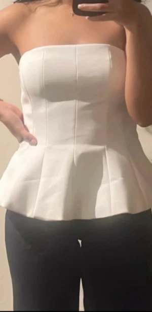 Superfin topp nyår - Säljer en vit axelbandslös topp med peplum och markerade sömmar. Toppen har en stilren och strukturerad form som ger en snygg siluett. Perfekt till fest eller nyår!