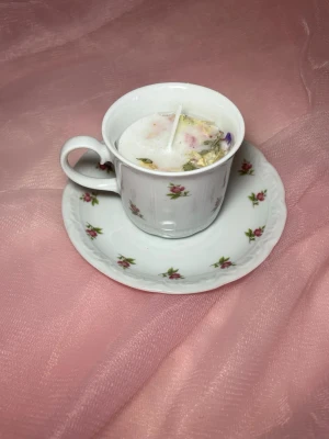 Doftljus i en tekopp i en vit färg med rosa blommor, med torkade blommor på nr 1 - Det här ljuset är gjort av återanvändbara material. Tekoppen är köpt secondhand och stearinet är från kyrkor som tänkte slänga det. Det här ljuset har en svag doft utav vanilj, så känsliga även kan använda det. Det här ljuset är även dekorerat med torkade blommor på och det finns fler utav samma design på hemsidan ifall att man vill ha sets.